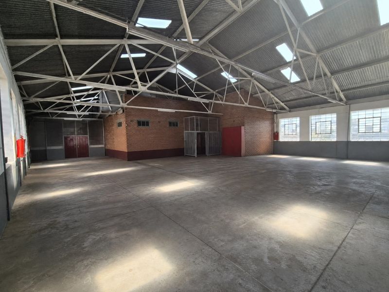 Spacious industrial warehouse featuring high exposed steel roof trusses, concrete flooring, abundant natural light from skylights, and secure internal partitioning.