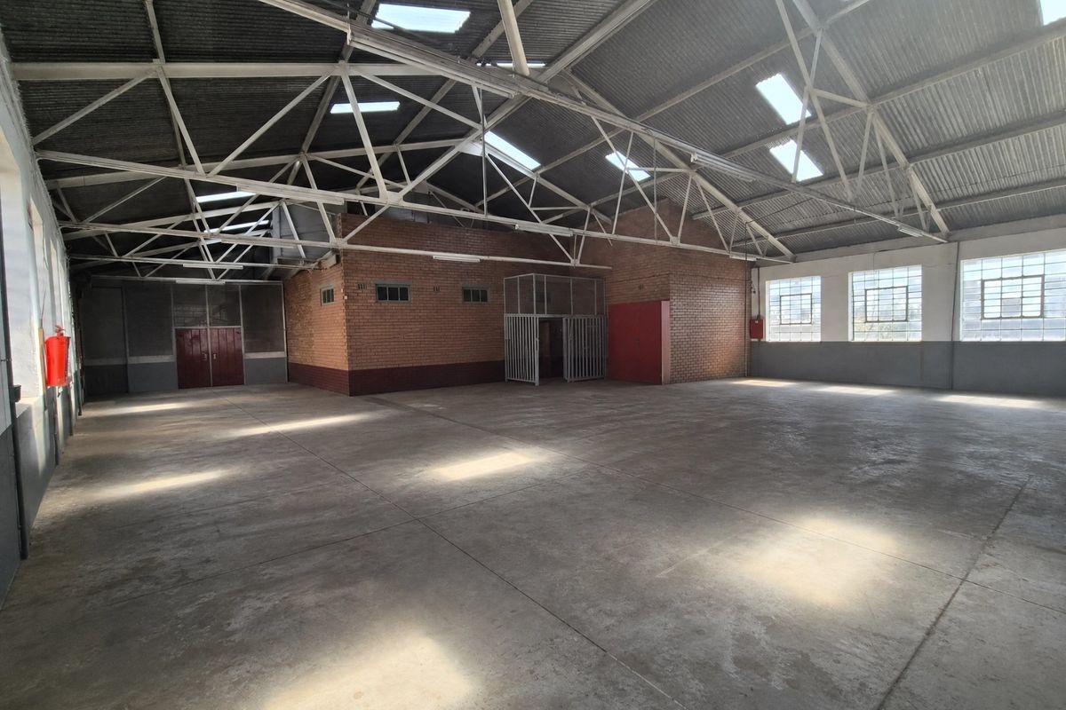 Spacious industrial warehouse featuring high exposed steel roof trusses, concrete flooring, abundant natural light from skylights, and secure internal partitioning.