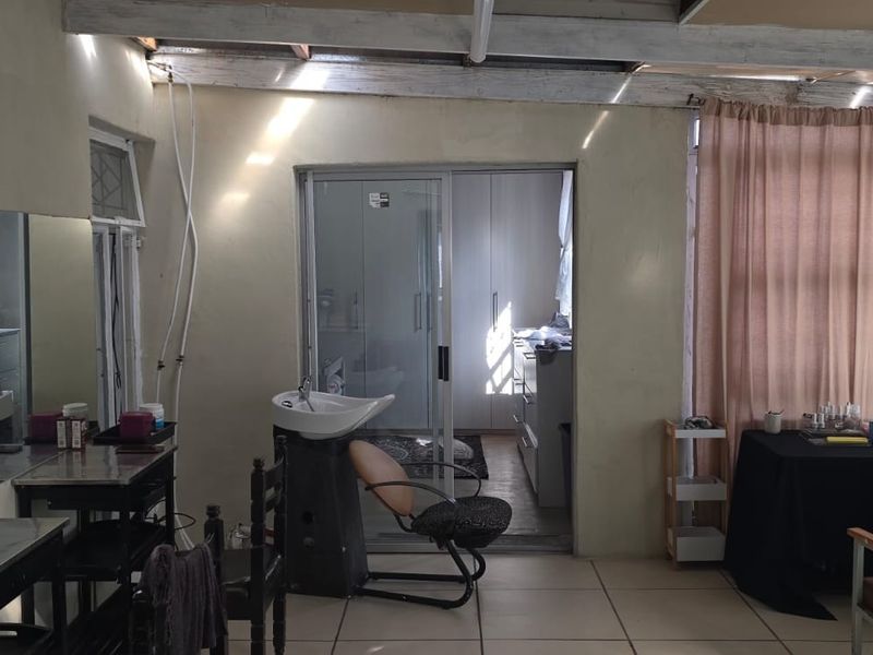 Utility space currently utilized as a salon, featuring tiled flooring, exposed ceiling beams, and direct access to an adjacent room via a sliding door.