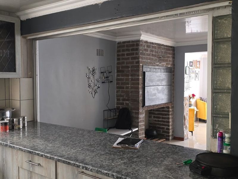 Kitchen featuring laminate countertops, built-in cabinetry, and a unique glass block feature wall, opening into a living area with a brick fireplace.