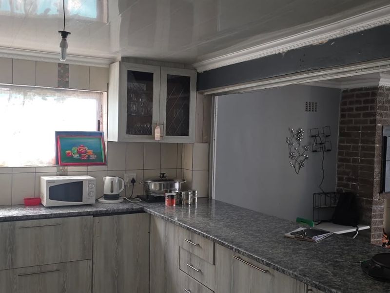 Kitchen featuring laminate cabinetry, granite-look countertops, and a pass-through window overlooking the adjacent living area with a brick fireplace.