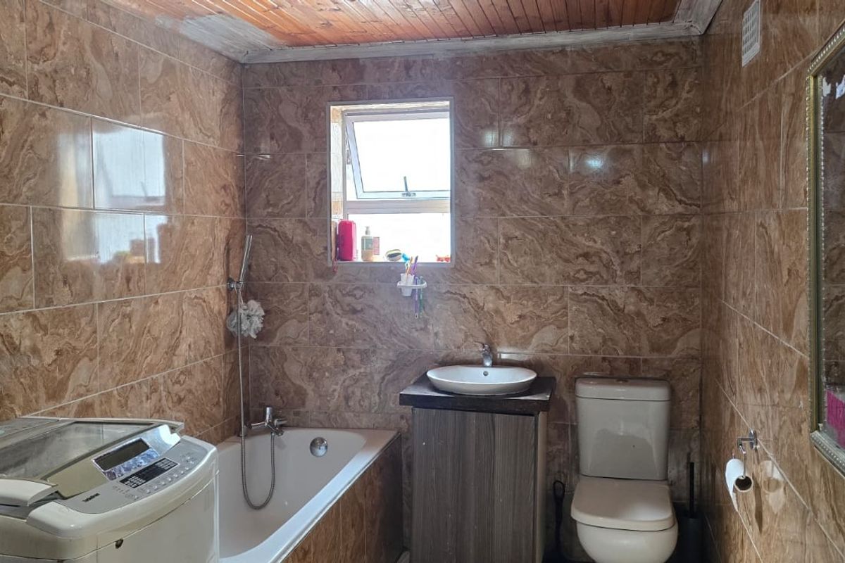 A bathroom featuring full-height marble-look wall tiles, a built-in bathtub with shower mixer, a vanity with vessel sink, and a timber-paneled ceiling.