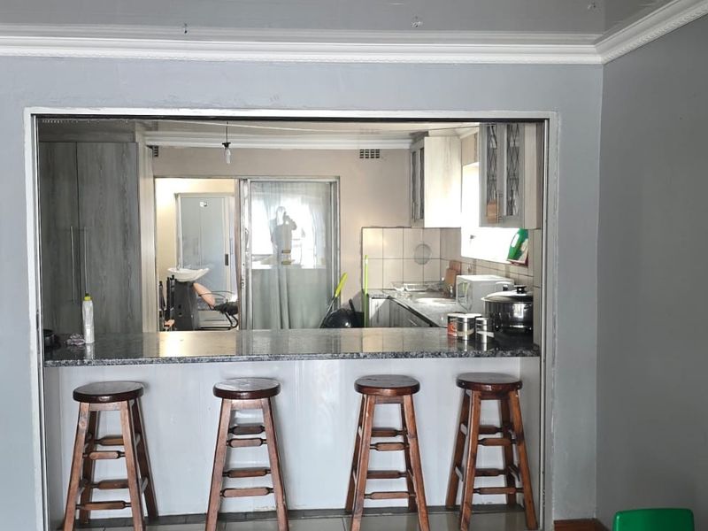 Open plan living area featuring a breakfast bar with granite countertops, connecting to a functional kitchen space with built-in cabinetry and tiled backsplash.