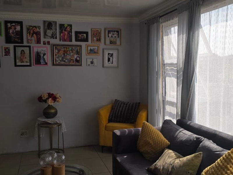 A comfortable living room featuring tiled flooring, coved ceilings, and a large window allowing for natural light.