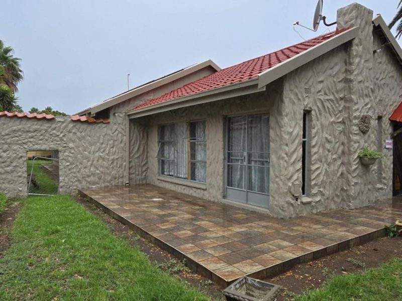 Rear view of the house featuring a tiled patio, textured plaster walls, and a red tiled roof with a sliding glass door entrance.