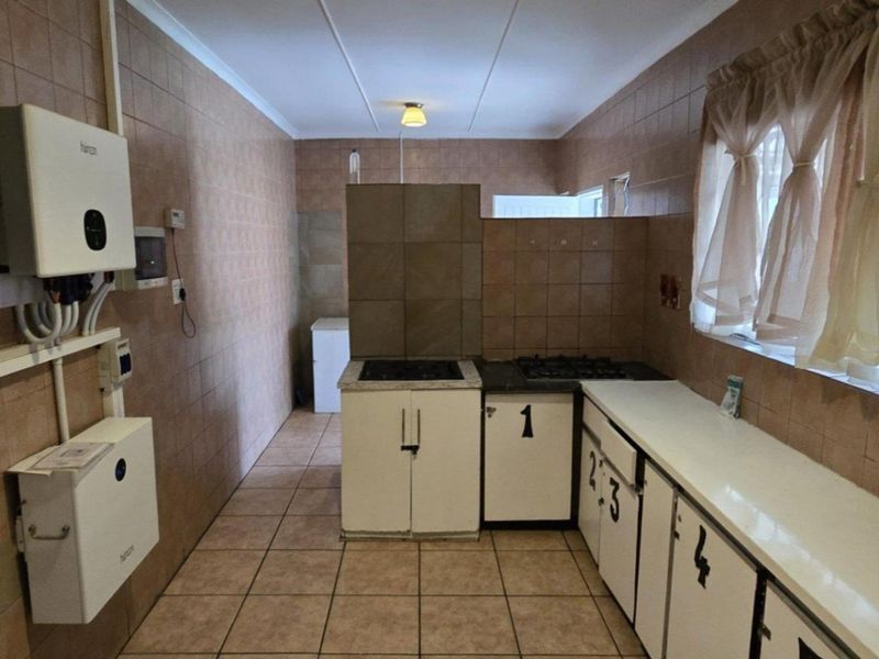 A functional kitchen featuring tiled walls and floors, built-in cabinetry, a gas hob, and an installed inverter system for power backup.