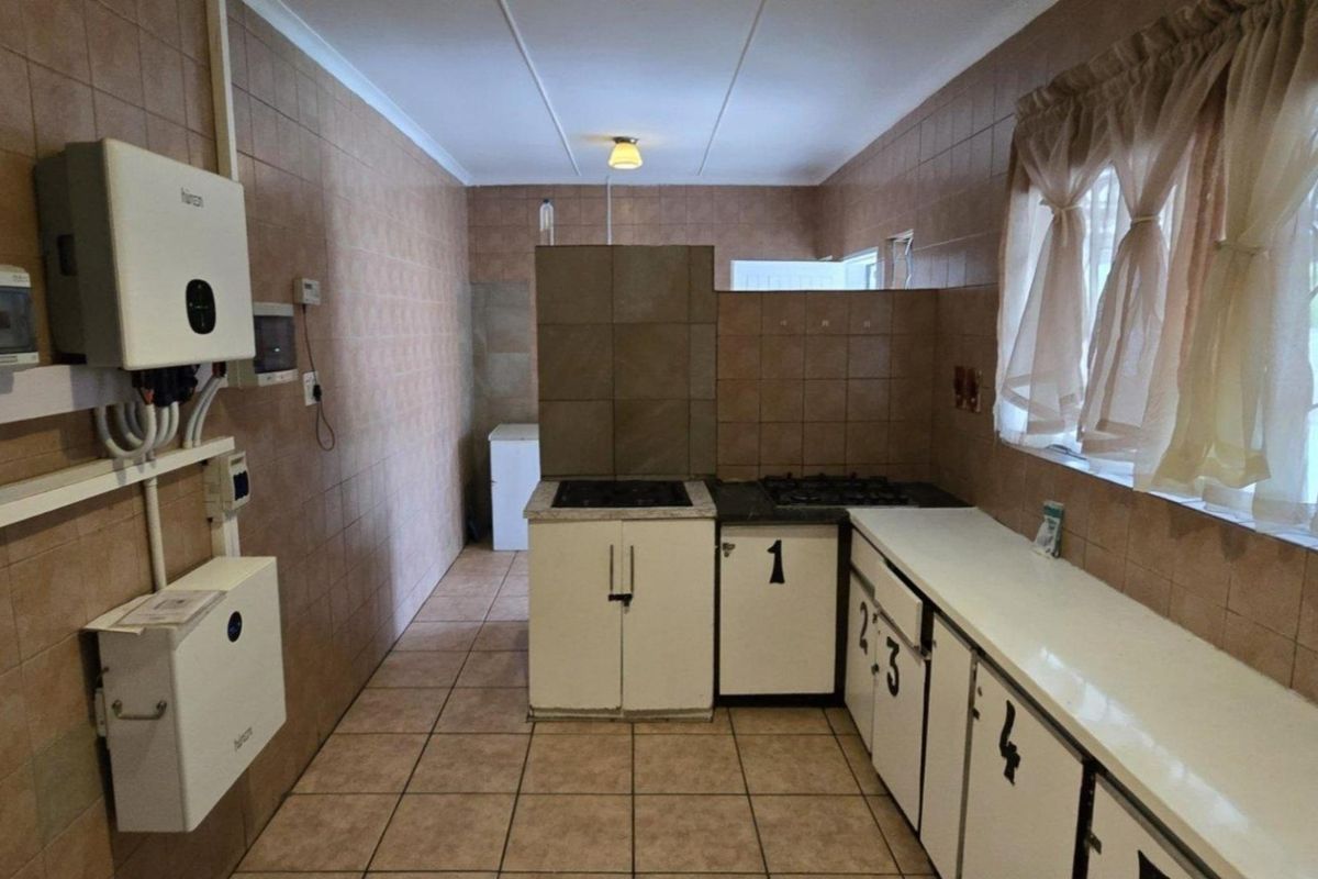 A functional kitchen featuring tiled walls and floors, built-in cabinetry, a gas hob, and an installed inverter system for power backup.
