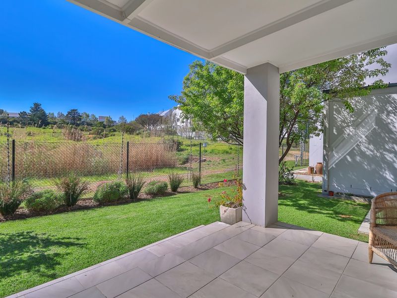A covered patio area with tiled flooring and a support pillar, overlooking a private garden and open landscape.