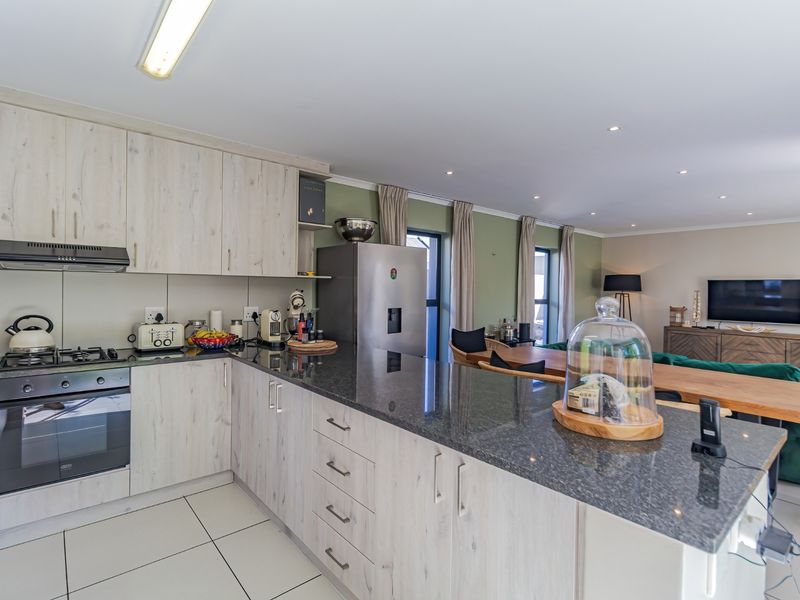 Modern open-plan kitchen featuring granite countertops, built-in appliances, and tiled flooring, seamlessly flowing into the adjacent dining and living area.