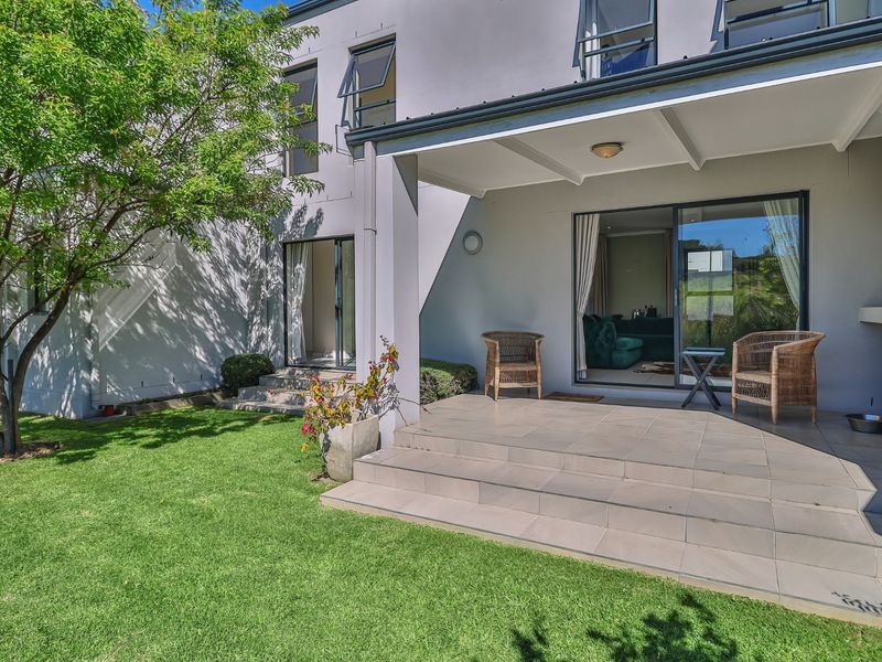 A well-maintained rear patio featuring tiled flooring, a built-in braai, and direct access to the garden through sliding glass doors.