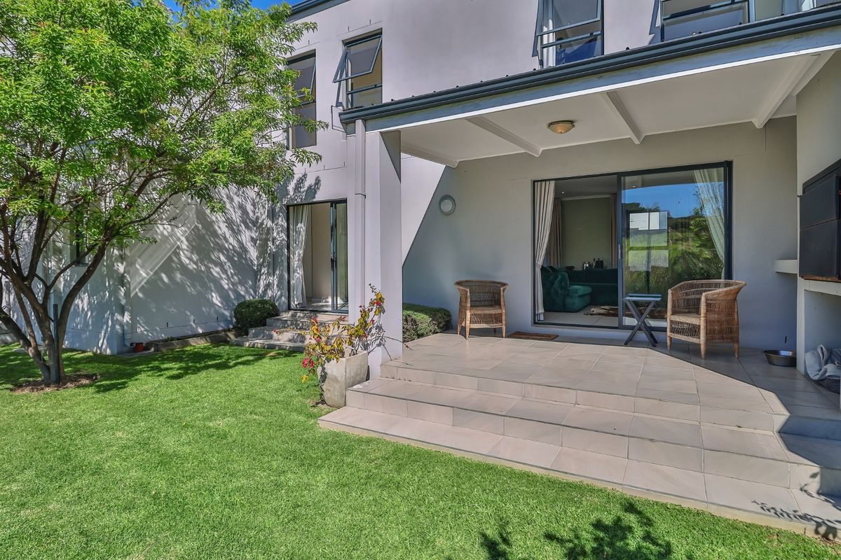 A well-maintained rear patio featuring tiled flooring, a built-in braai, and direct access to the garden through sliding glass doors.