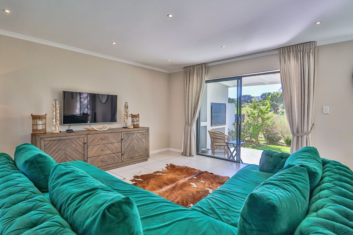 A bright living room featuring tiled flooring, recessed downlights, and a large sliding glass door providing direct access to the outdoor patio and garden.
