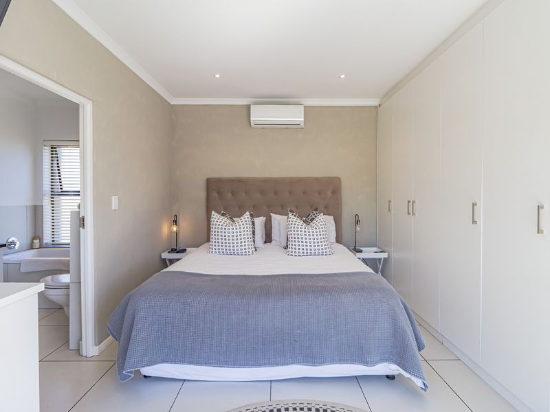 A well-maintained bedroom featuring built-in cupboards, tiled flooring, and a wall-mounted air conditioning unit, with an adjoining en-suite bathroom.