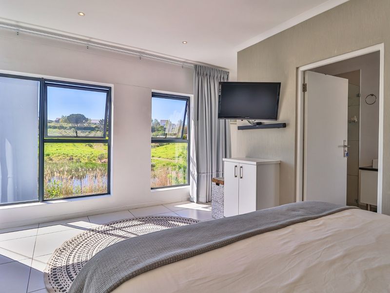 A bright bedroom featuring tiled flooring, recessed lighting, and large aluminium windows offering scenic views, with direct access to an en-suite bathroom.