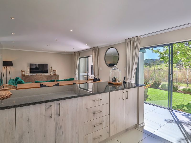 Spacious open-plan living area featuring a modern kitchen island with granite countertops, recessed lighting, and large sliding glass doors leading to the garden.