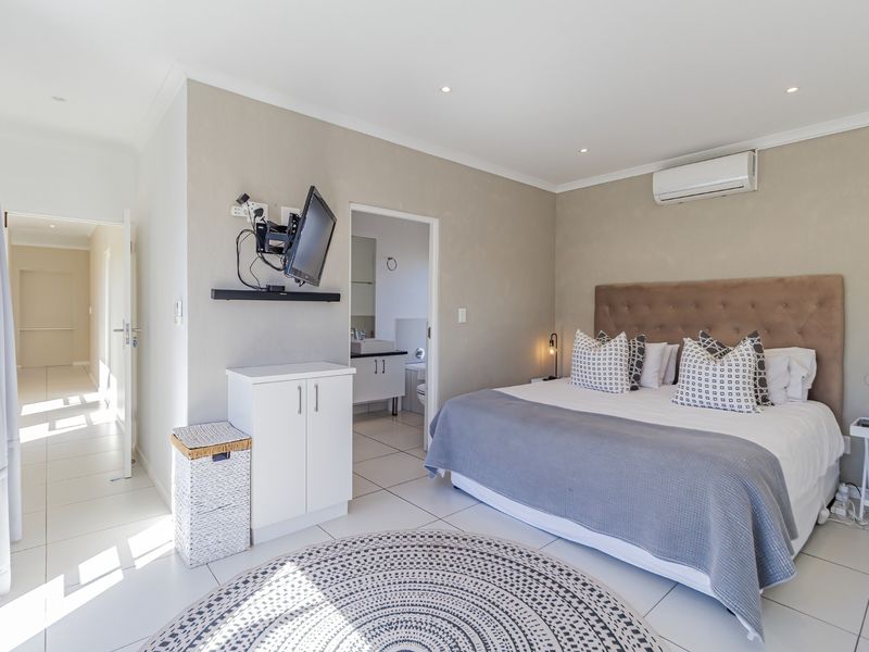 A well-maintained bedroom featuring tiled flooring, recessed lighting, a wall-mounted air conditioning unit, and direct access to an en-suite bathroom.