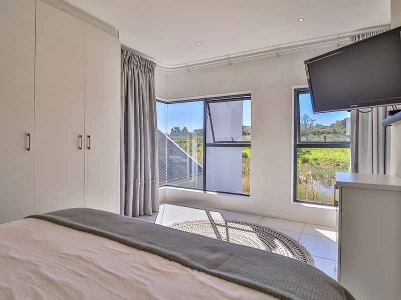 A bright bedroom featuring built-in cupboards, tiled flooring, recessed lighting, and large windows offering scenic views.