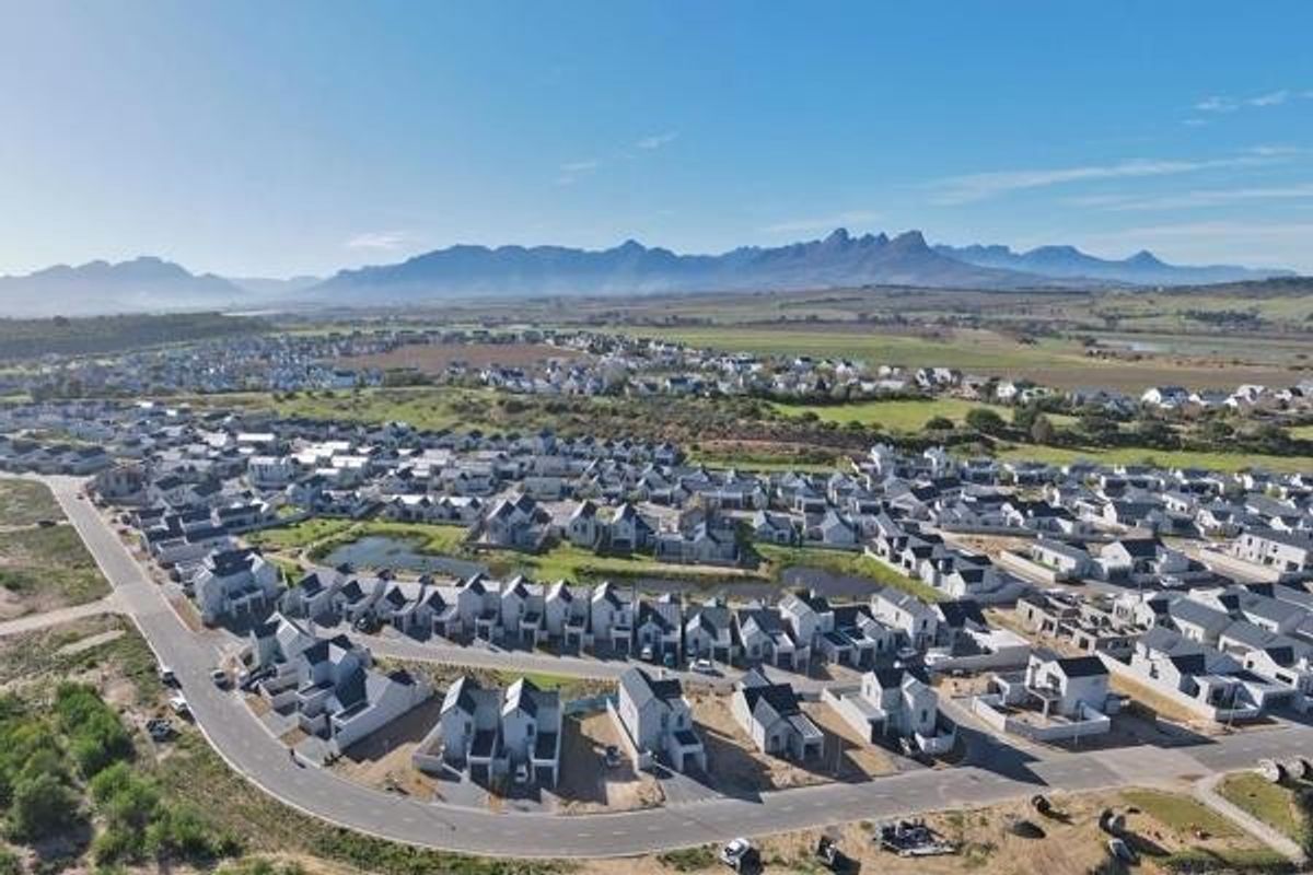 An aerial view of a residential estate featuring modern housing units, paved streets, and scenic mountain views in the background.