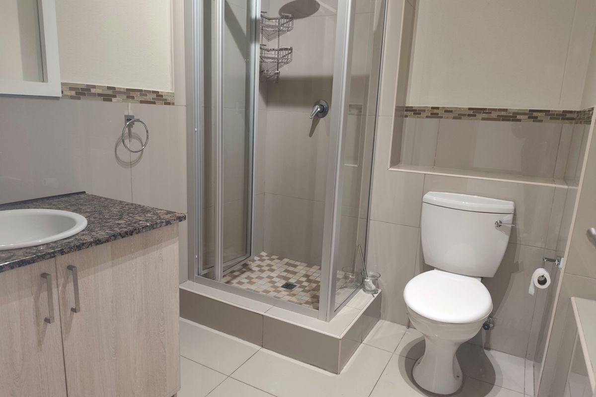 A clean and functional bathroom featuring a vanity with granite countertop, a glass-enclosed shower, and neutral wall and floor tiling.
