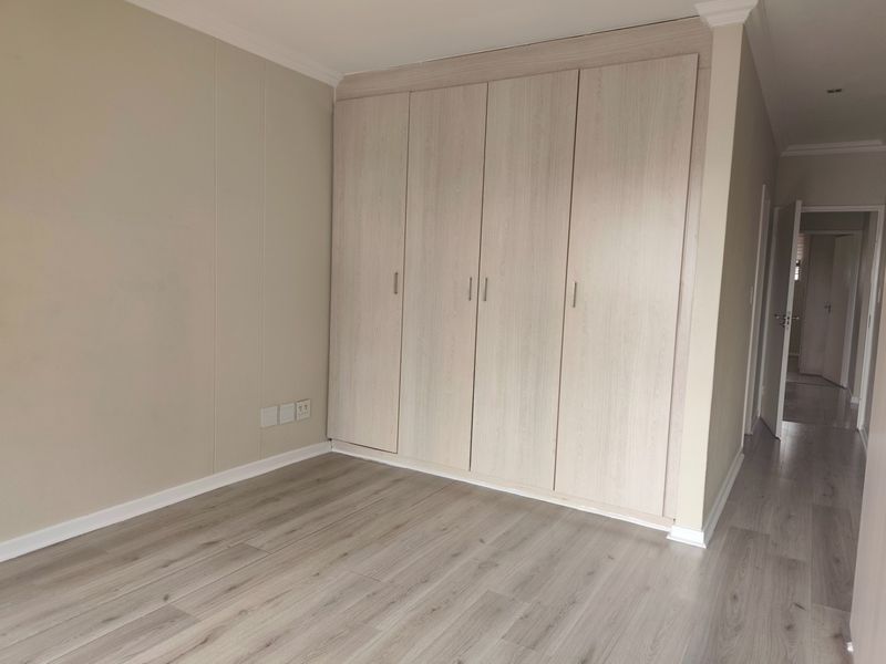A bright, empty bedroom featuring modern light-wood laminate flooring and spacious built-in cupboards with a neutral color palette.