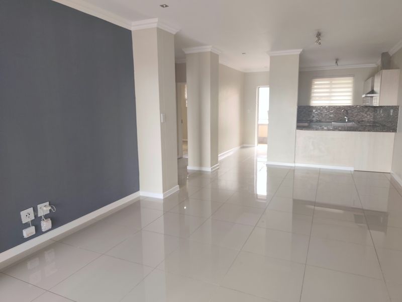 Spacious open-plan living area featuring polished porcelain tiles, neutral walls with a feature wall, and a modern kitchen with granite countertops.