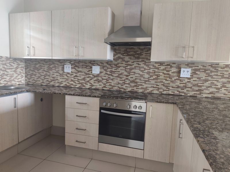 Modern kitchen featuring light wood-finish cabinetry, granite countertops, a mosaic tile backsplash, and integrated stainless steel appliances including an oven and extractor fan.