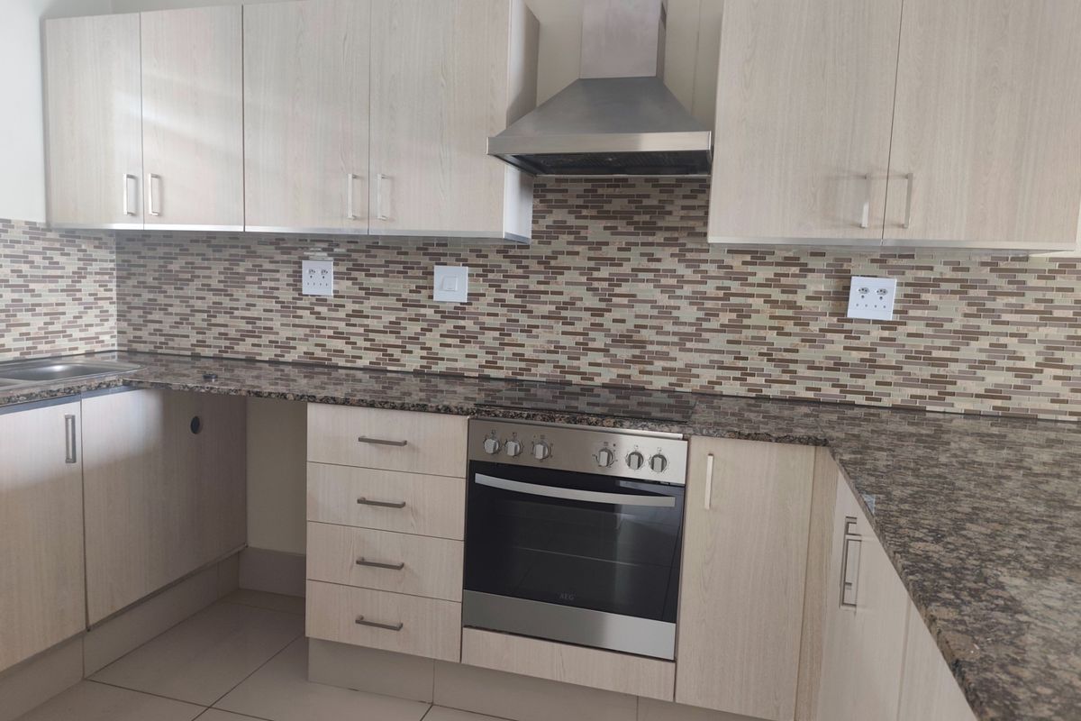 Modern kitchen featuring light wood-finish cabinetry, granite countertops, a mosaic tile backsplash, and integrated stainless steel appliances including an oven and extractor fan.
