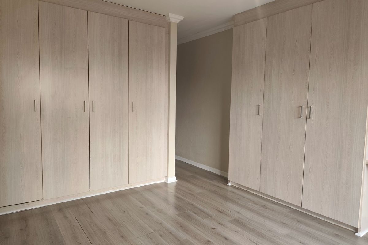 A bright bedroom featuring extensive built-in cupboards with light wood-grain finish and modern laminate flooring throughout.