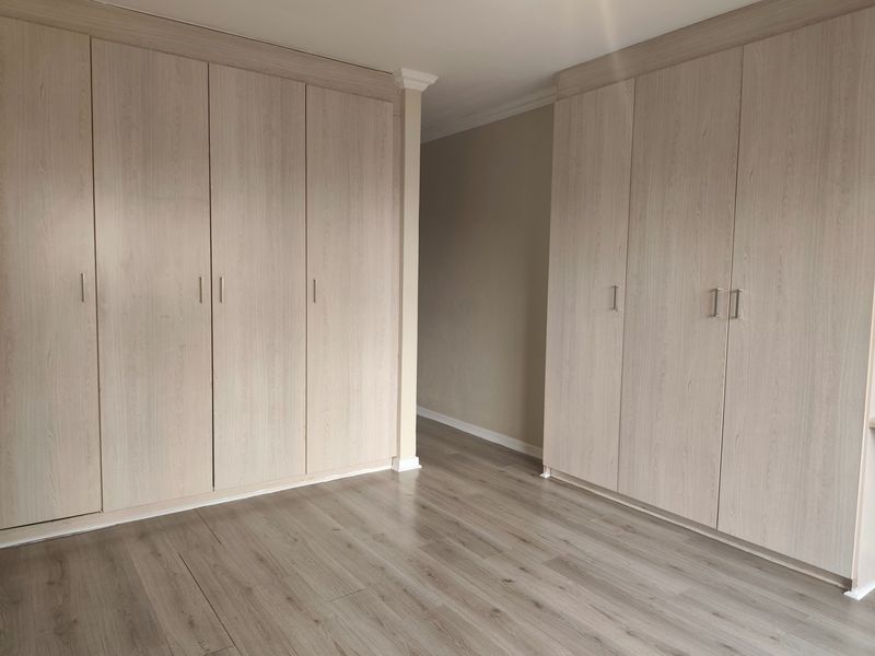 A bright bedroom featuring extensive built-in cupboards with light wood-grain finish and modern laminate flooring throughout.