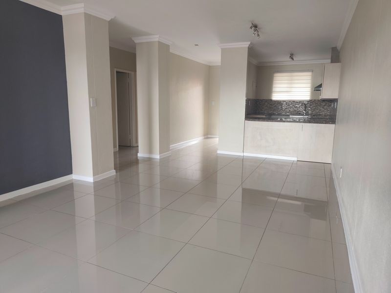 Spacious open-plan living area featuring polished tile flooring, neutral walls, and a functional kitchen with granite countertops and built-in cabinetry.