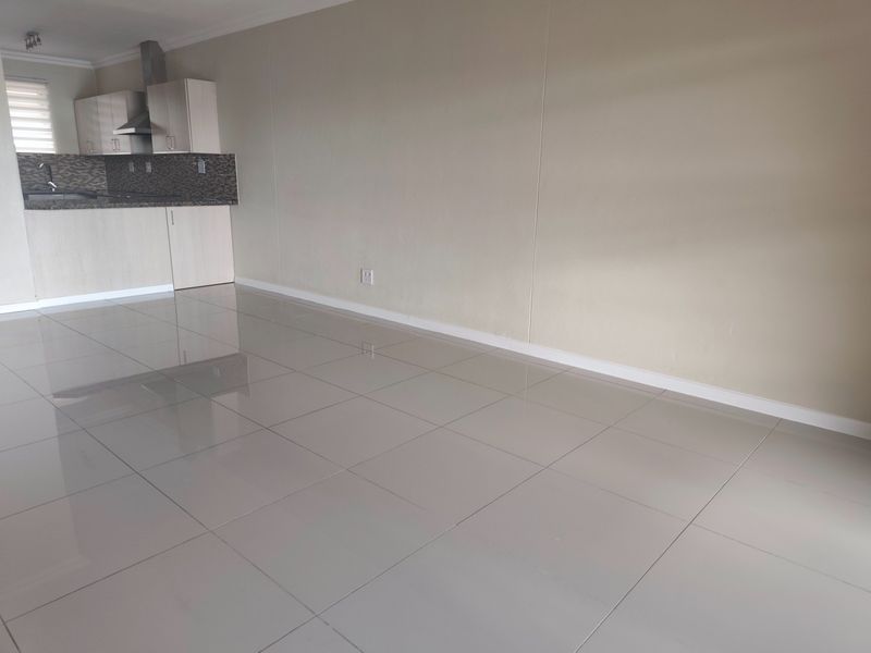 An open-plan living and kitchen area featuring neutral tiled flooring, modern cabinetry, and a built-in extractor fan in a clean, vacant space.