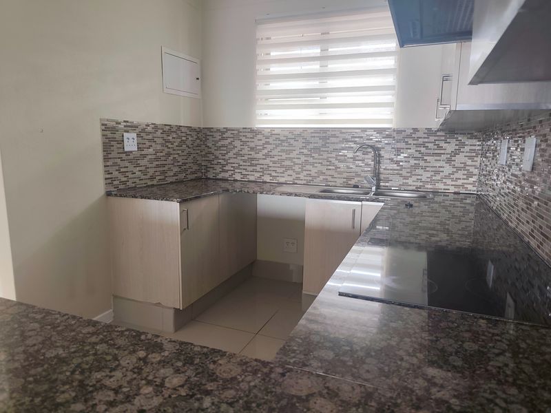 A clean, functional kitchen featuring granite countertops, mosaic tile backsplash, built-in electric hob, and ample cabinetry for storage.