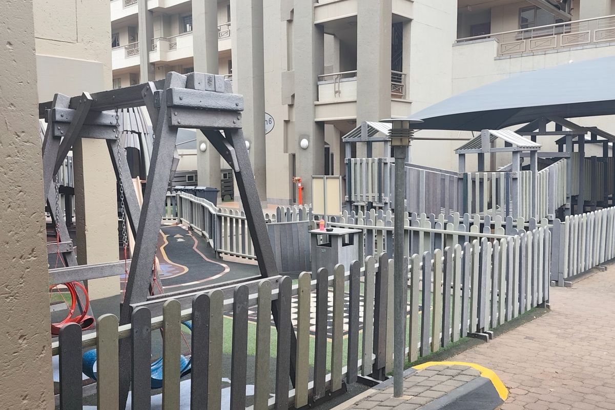 A communal playground area located within the apartment complex, featuring fixed play structures, safety surfacing, and perimeter fencing.