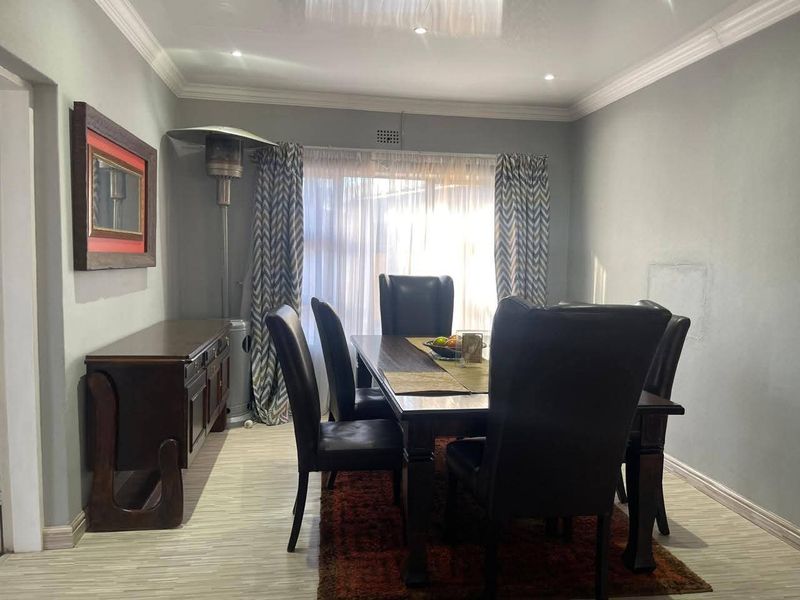 A dining room featuring laminate flooring, recessed downlighting, and crown molding, with visible wall repair marks requiring cosmetic attention.
