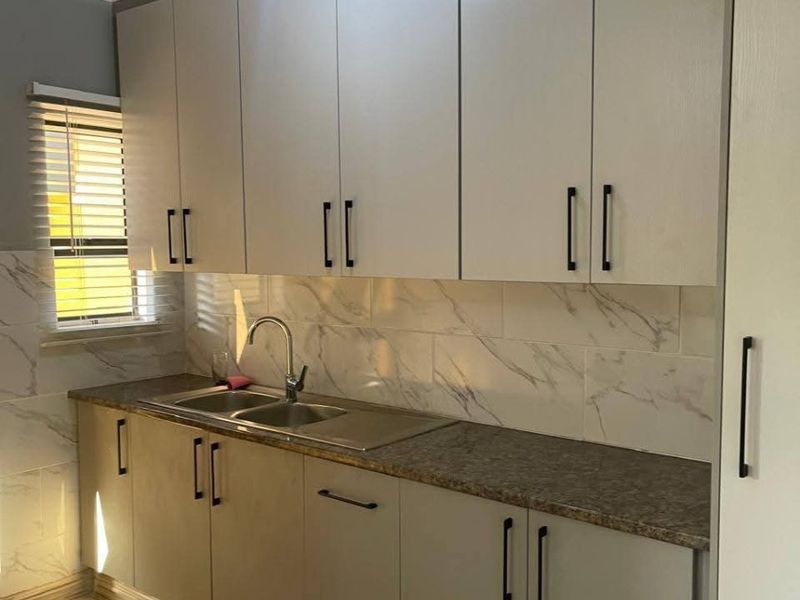 A clean, modern kitchen featuring light grey cabinetry, marble-look tile backsplash, stainless steel sink, and wood-look flooring.