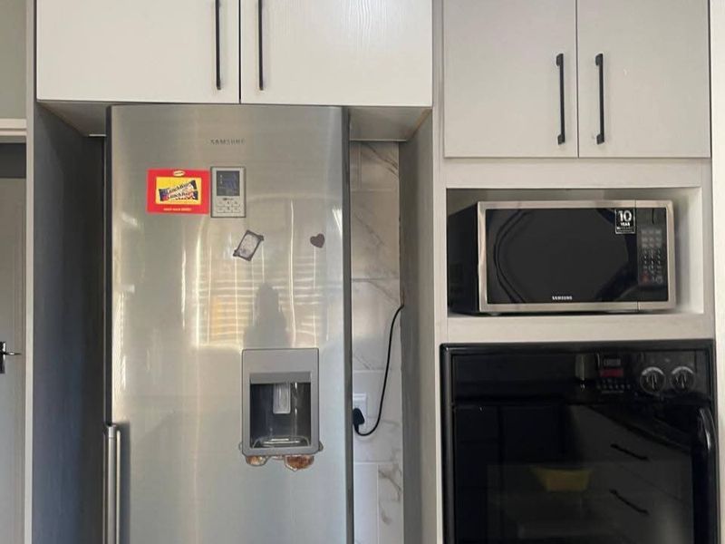 A modern kitchen section featuring built-in cabinetry, a wall-mounted oven, and a built-in microwave with a tiled splashback.