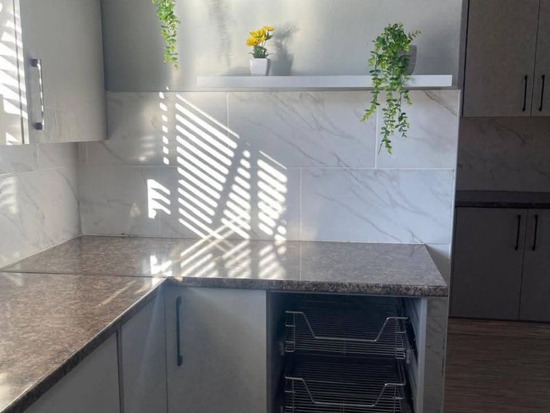A modern kitchen area featuring marble-effect tiled backsplash, laminate countertops, built-in cabinetry, and convenient pull-out wire storage drawers.