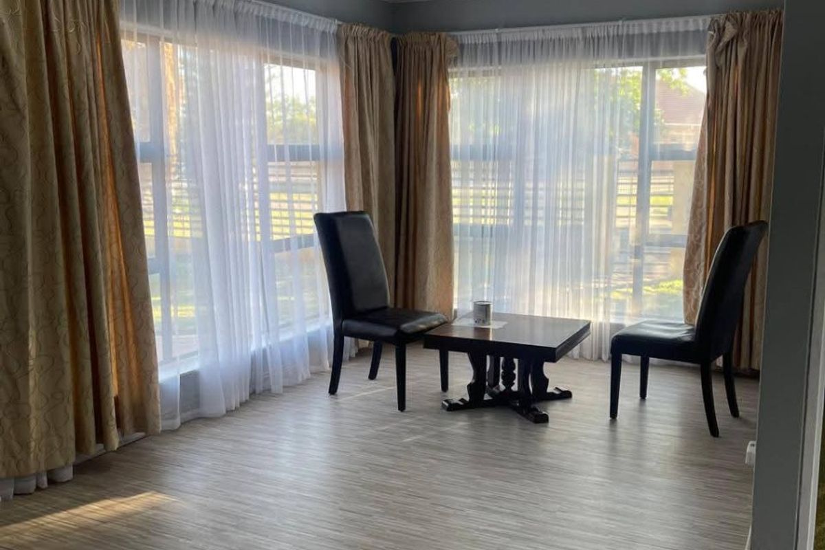 A bright living area featuring modern laminate flooring, a glossy stretch ceiling, and large windows that provide ample natural light.