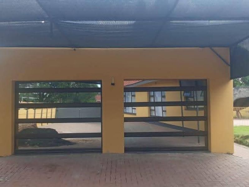 A double garage featuring modern horizontal-slat doors, protected by a large shade cloth carport structure over a paved driveway area.