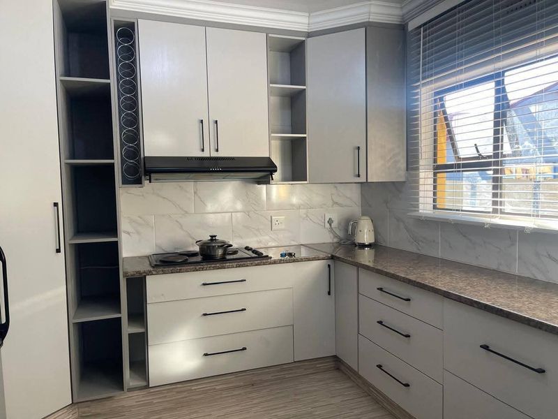 Modern kitchen featuring light grey cabinetry, stone-look countertops, marble-effect tiled backsplash, built-in electric hob with extractor fan, and ample storage space.