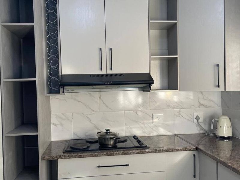 Modern kitchen featuring light grey cabinetry, granite countertops, marble-look tile backsplash, and integrated hob with extractor fan.