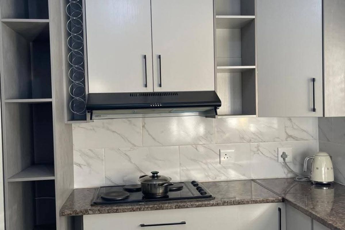 Modern kitchen featuring light grey cabinetry, granite countertops, marble-look tile backsplash, and integrated hob with extractor fan.