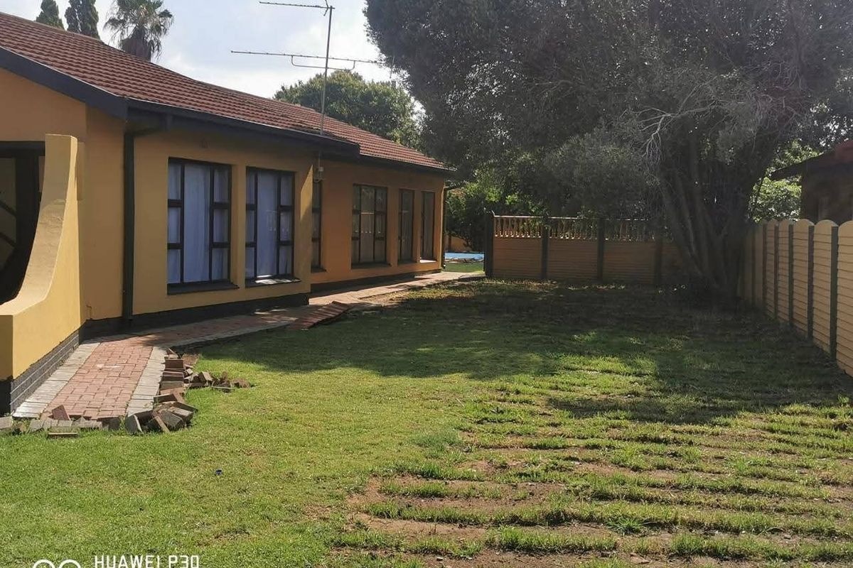 Rear view of the house showing a paved walkway, lawn area, and perimeter walling.