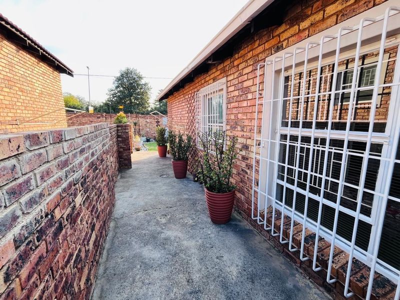 A side walkway featuring face brick walls, security bars on windows, and a concrete path leading to the rear garden area.