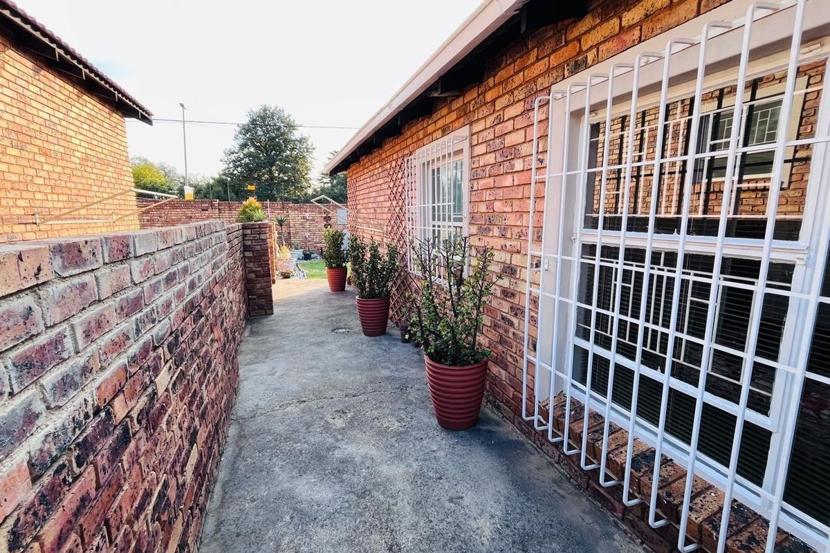 A side walkway featuring face brick walls, security bars on windows, and a concrete path leading to the rear garden area.