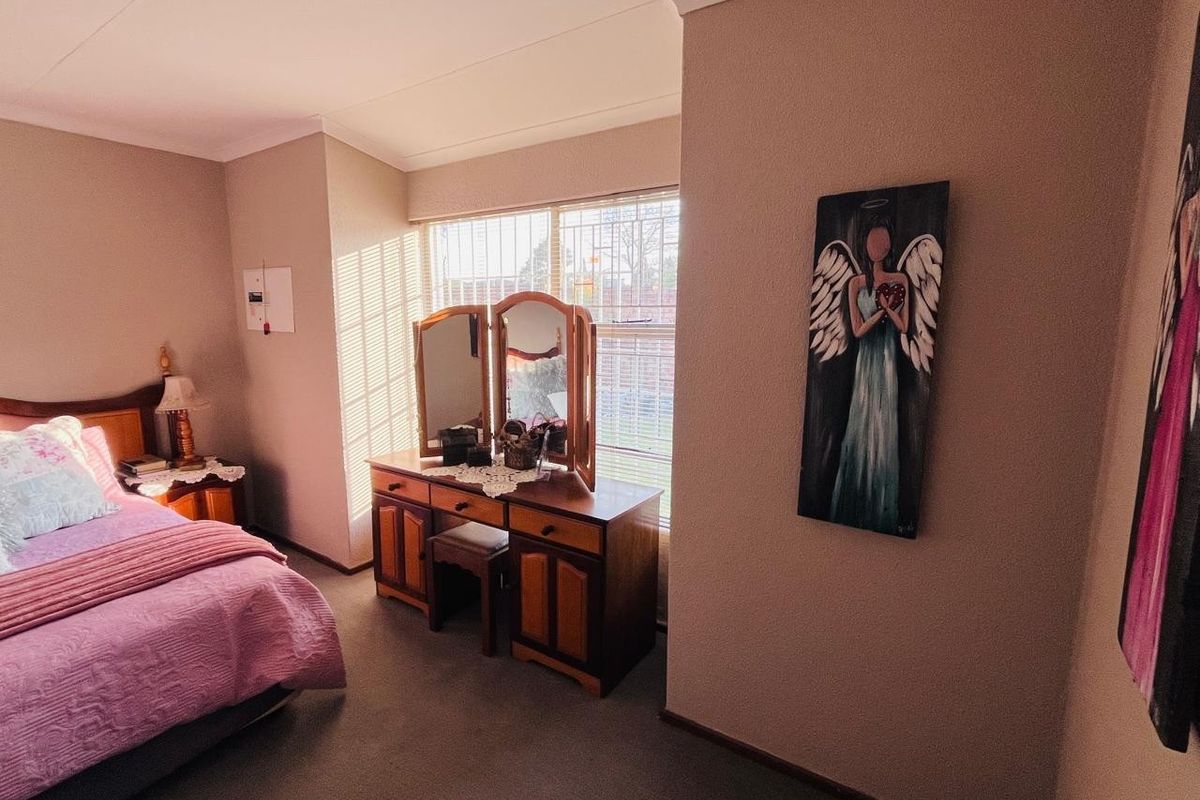 A well-lit bedroom featuring neutral wall tones, carpeted flooring, and large windows fitted with security bars.