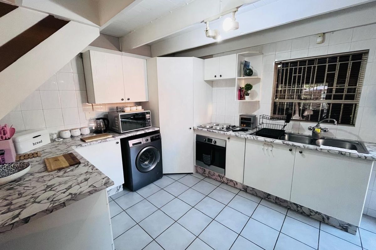 Functional kitchen featuring white cabinetry, marble-effect countertops, built-in oven and hob, tiled flooring, and a window with security bars.