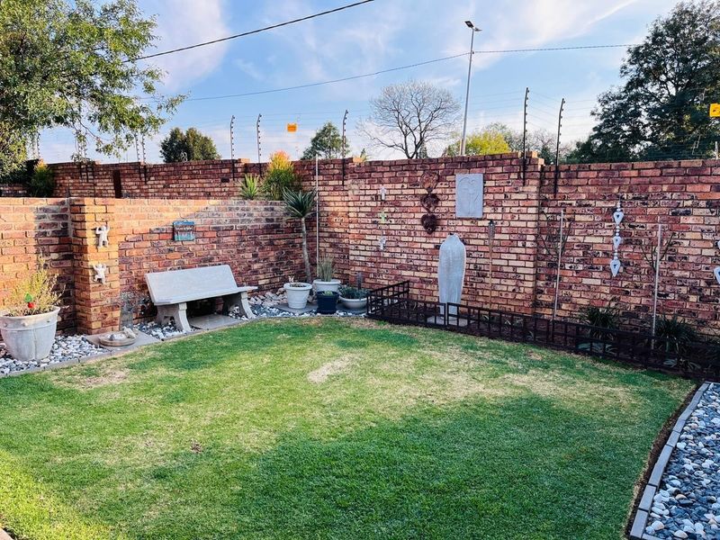 A well-maintained private garden featuring a lush lawn, decorative pebble borders, and a secure brick boundary wall with integrated electric fencing.