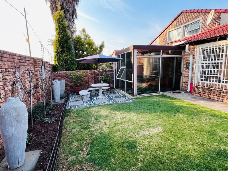 A well-maintained rear garden featuring a lawn, brick boundary walls with electric fencing, and an enclosed patio area with security bars.