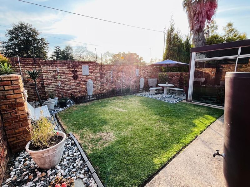 A private rear garden featuring a well-maintained lawn, brick boundary walls, and a paved area with an attached enclosed patio structure.
